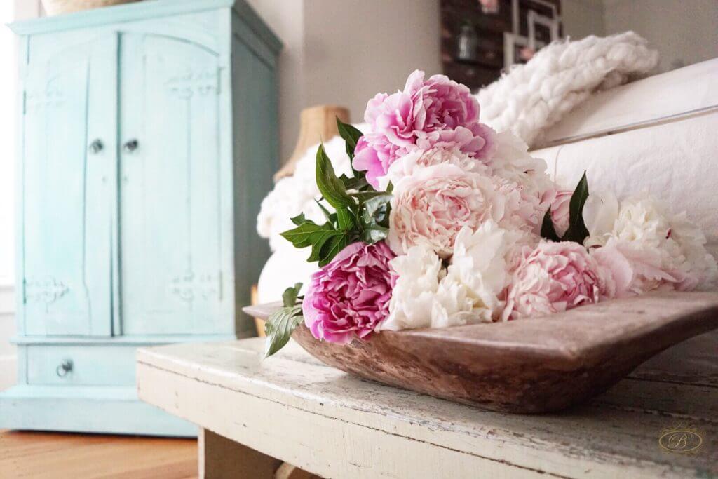 A bundle of peonies laying in a salvaged dough bowl on top of a vintage bench.