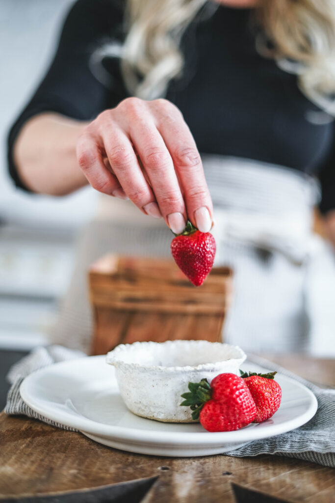 A fresh strawberry about to be dipped in chocolate.