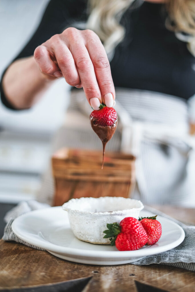 Letting chocolate drip from a strawberry that has just been dipped.