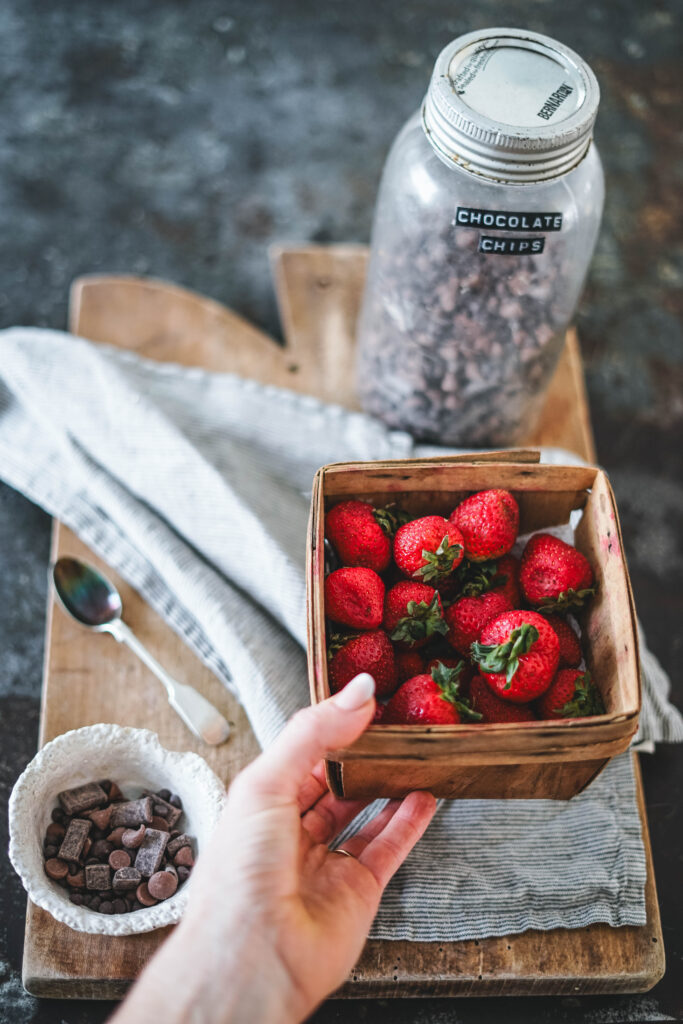 Strawberries, chocolate chips in a jar which are the ingredients required for making dark chocolate dipped strawberries. 