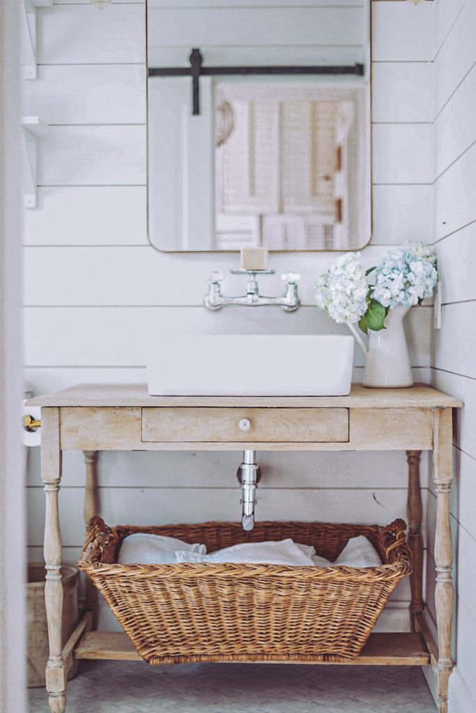 Farmhouse bathroom with shiplap walls and an antique basket used for storage and organization. Ideas for small spaces.