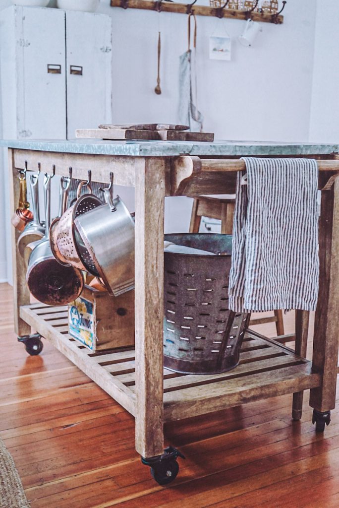 Rustic farmhouse kitchen island with a striped linen towel and copper pots hanging on the side for storage.