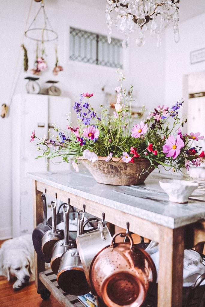 Farmhouse kitchen with flowers and copper pots hanging on the side of the island.