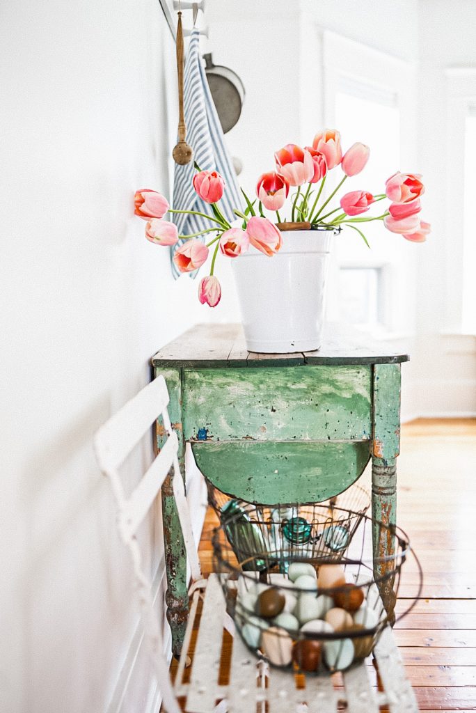 White vintage enamel bucket on a green antique table with spring tulip flowers