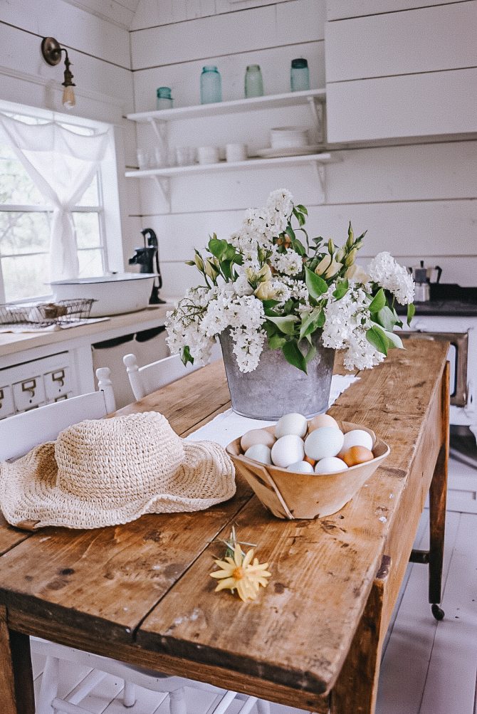 a woven garden hat, farm fresh coloured eggs and white lilacs on a harvest table in a shed house