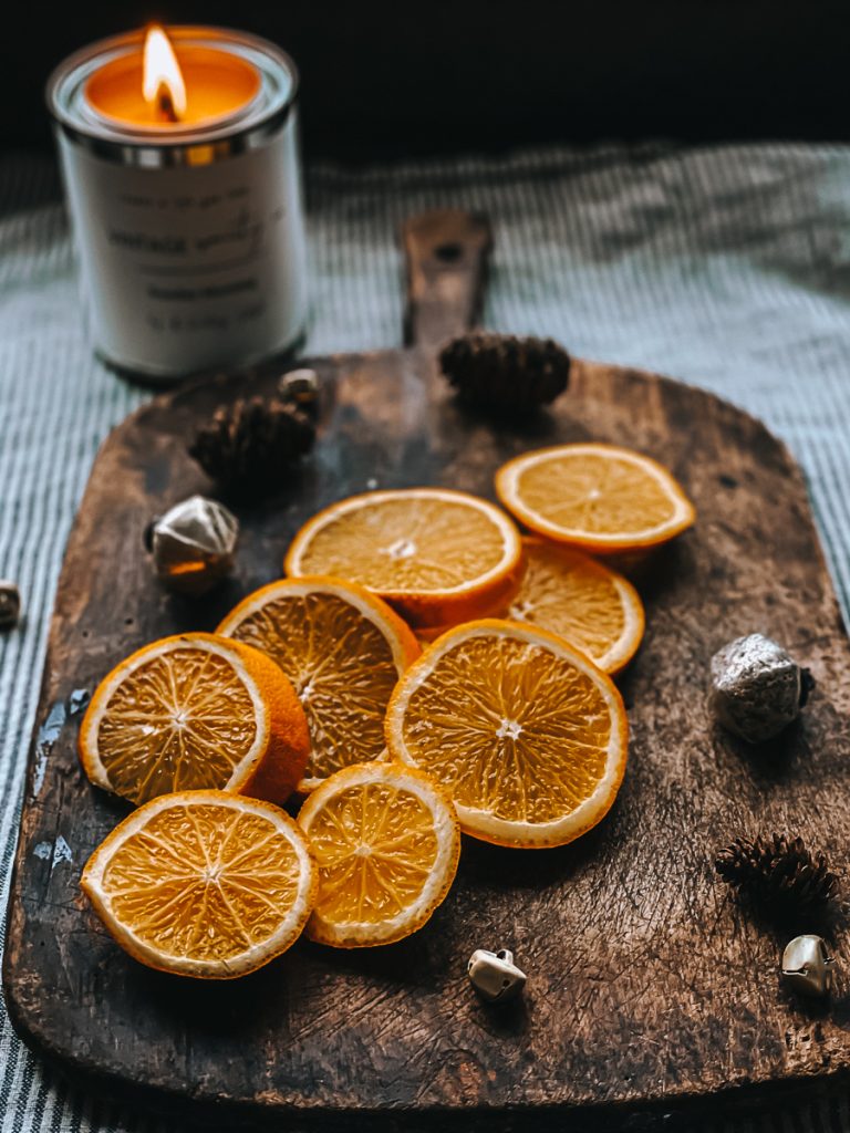 dried orange slices on a vintage cutting board with brass bells and pine cones.