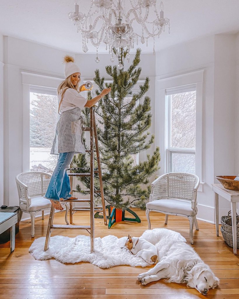 girl decorating a large pine minimal Christmas tree in a living room