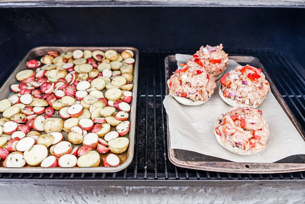 Stuffed portobello mushrooms on a tray on the smoker with roasted potatoes.