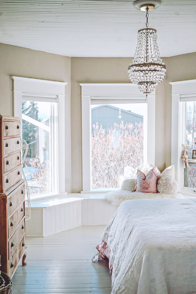 White window bench in a bay window of a bedroom. Pillows on top of the window seat.