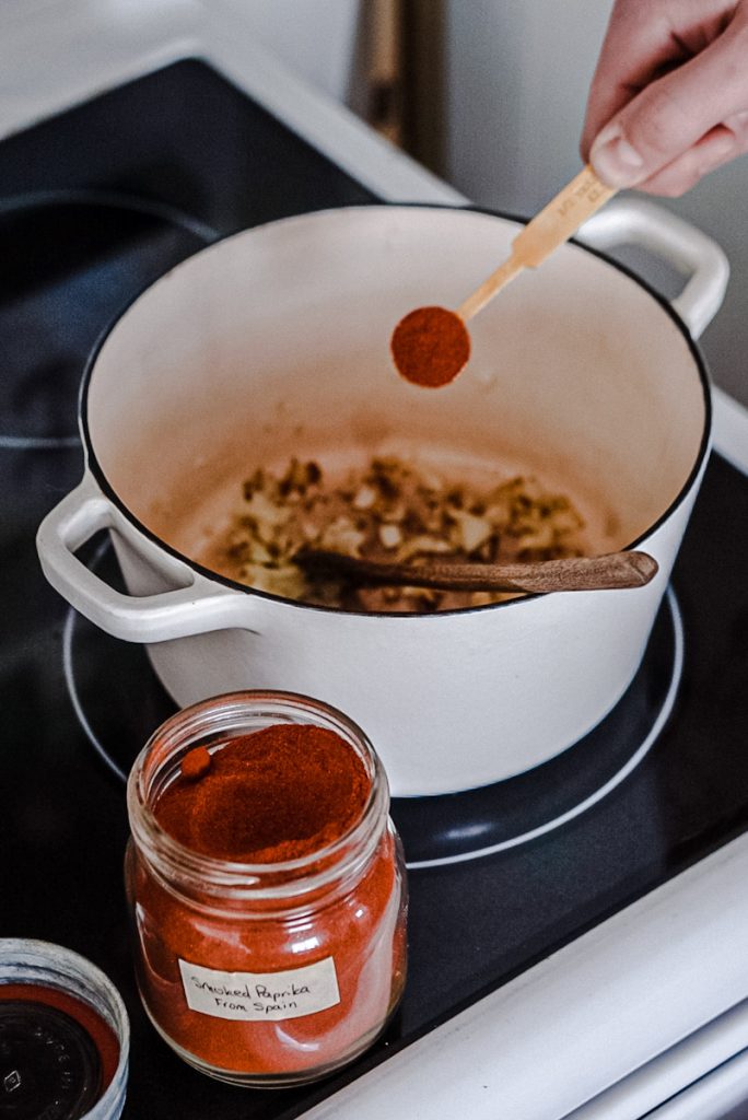 Adding smoked paprika to a pot to make tomato soup.