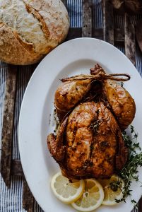a whole smoked chicken with lemon and thyme on a platter with a fresh loaf of bread
