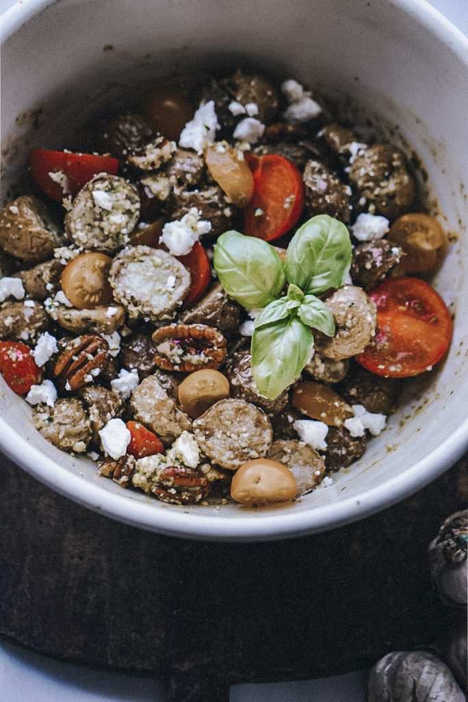 finished pesto potato salad with goat cheese, pecans and tomatoes in a bowl