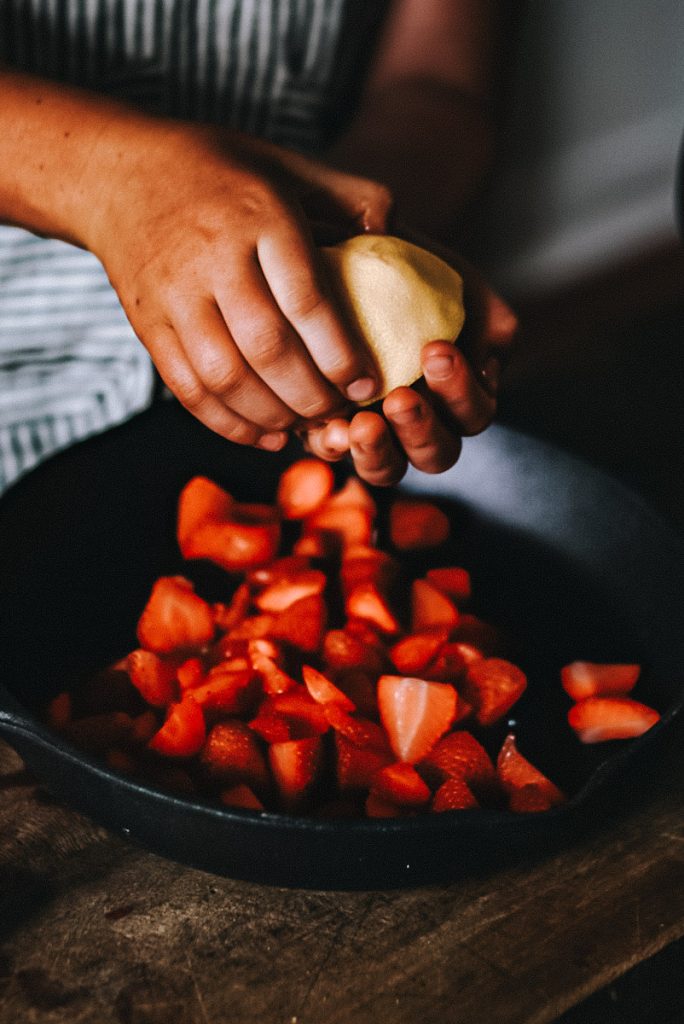 adding lemon to strawberries in a pan to make strawberry cheesecake topping
