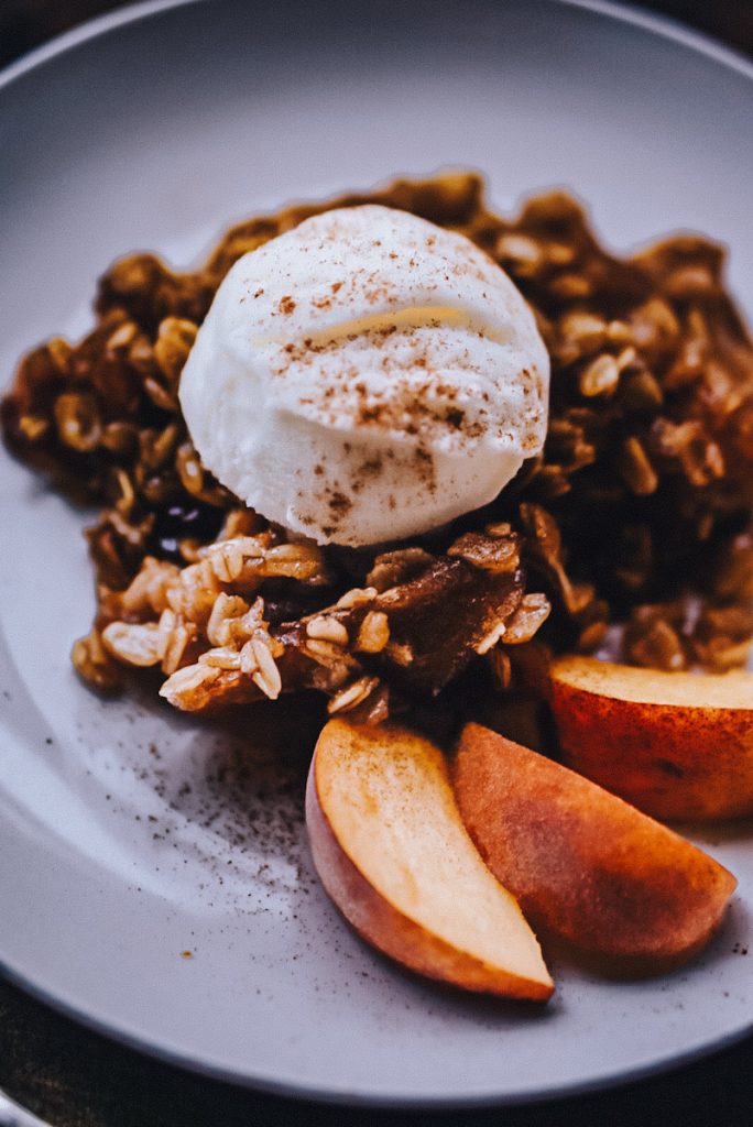 crunchy peach crumble with vanilla ice cream and sliced peaches on a white plate