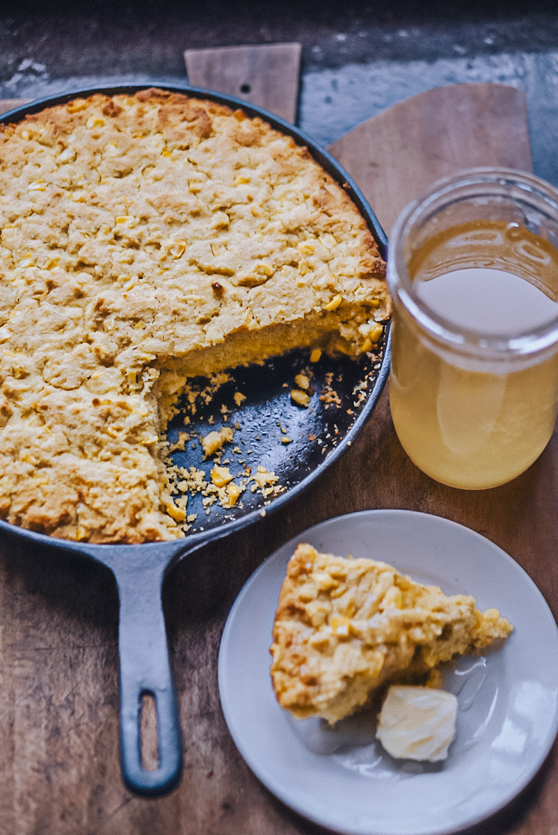 Cast iron skillet cornbread that has been sliced and placed on a plate with honey and butter.