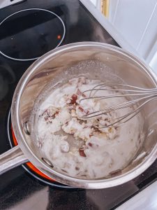 Thickening Béchamel using a whisk in a pot on the stove.