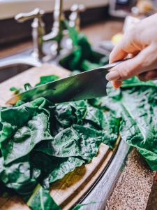 Chopping Swiss chard on a cutting board with a kitchen knife.