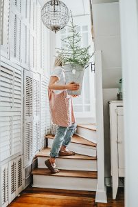 Deborah McDonald, B Vintage Style walking up the back staircase with a linen apron on and carrying a small Christmas tree.