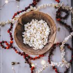 Strands of strung cranberries and popcorn garland beside a large bowl of popcorn.