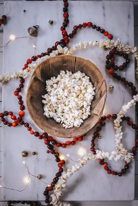 Strands of strung cranberries and popcorn garland beside a large bowl of popcorn.