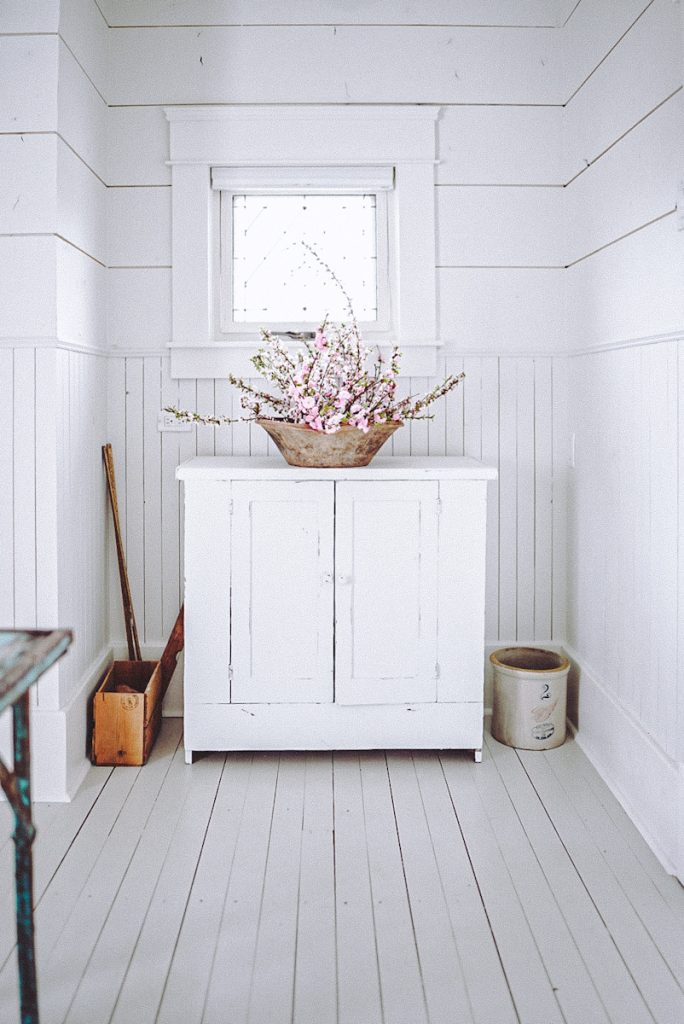 A beautiful space with vertical and horizontal shiplap and a white antique cabinet with wood accents and farmhouse decor around it.