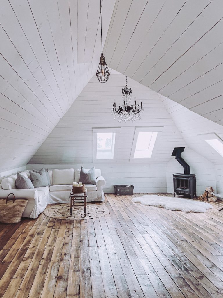 A beautiful attic space that has been made into a family room with a slip cover sofa, round area rug and a black woodstove.