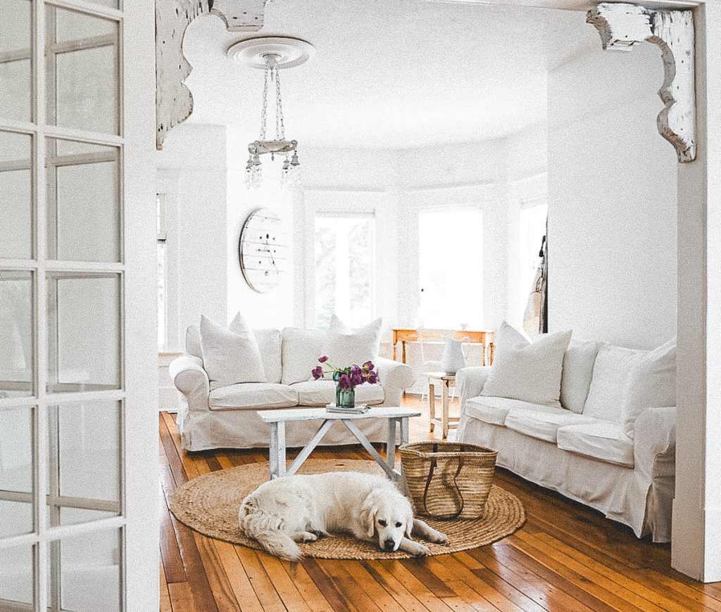 A bright family room that has two slipcover sofas and a large spool clock on the wall.