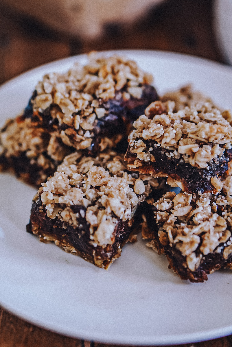 Delicious date slice bars that are stacked on top of each other on a white plate.