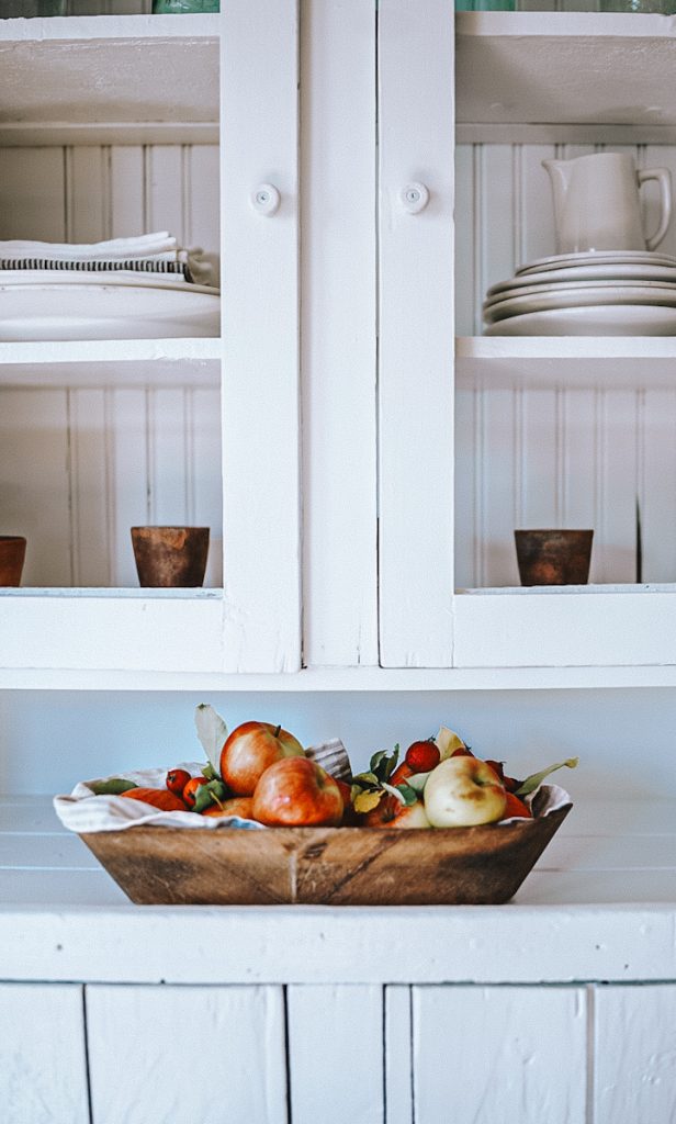 A beautiful antique wooden bowl holding apples on a kitchen counter and organized cabinets.