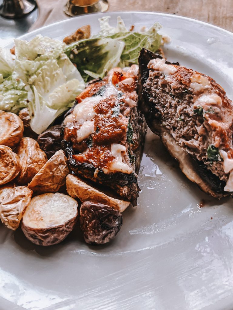 Stuffed portobello mushroom that is cut in half and plated with a Caesar salad and potatoes.