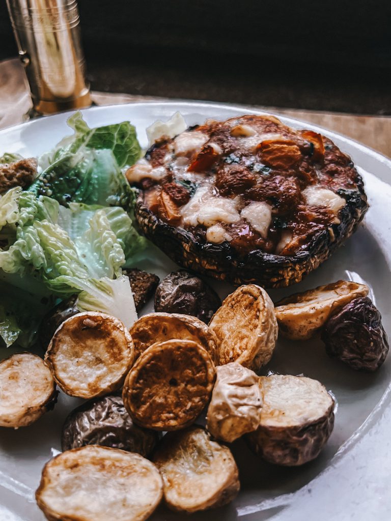 Portobello stuffed mushroom that has herbs and goat cheese on a plate with Caesar salad and roasted potatoes.