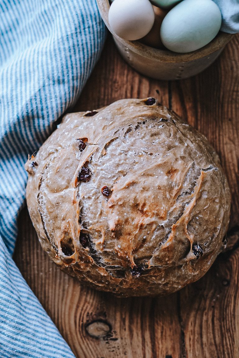 A fresh loaf of raisin bread that has just cooled on a cutting board.