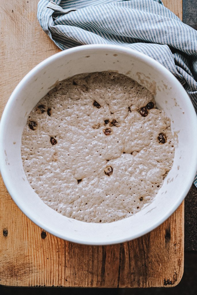 Bread dough with cinnamon and raisins that is rising in a large mixing bowl.