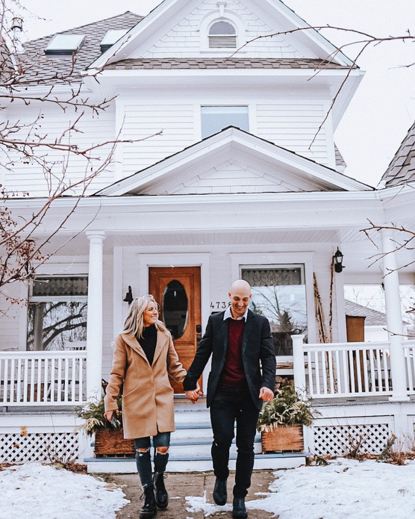 A beautiful white victorian house with a couple walking in front holding hands and smiling.