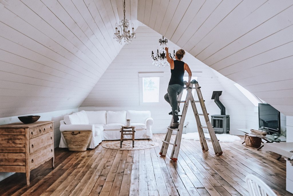 A lady standing on a ladder hanging a light fixture in a home remodel