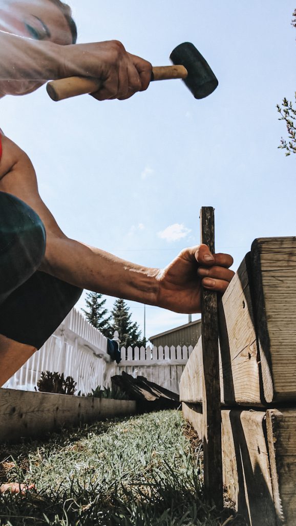 Deborah from B Vintage Style hammering a stake into the ground to make a wattle fence.