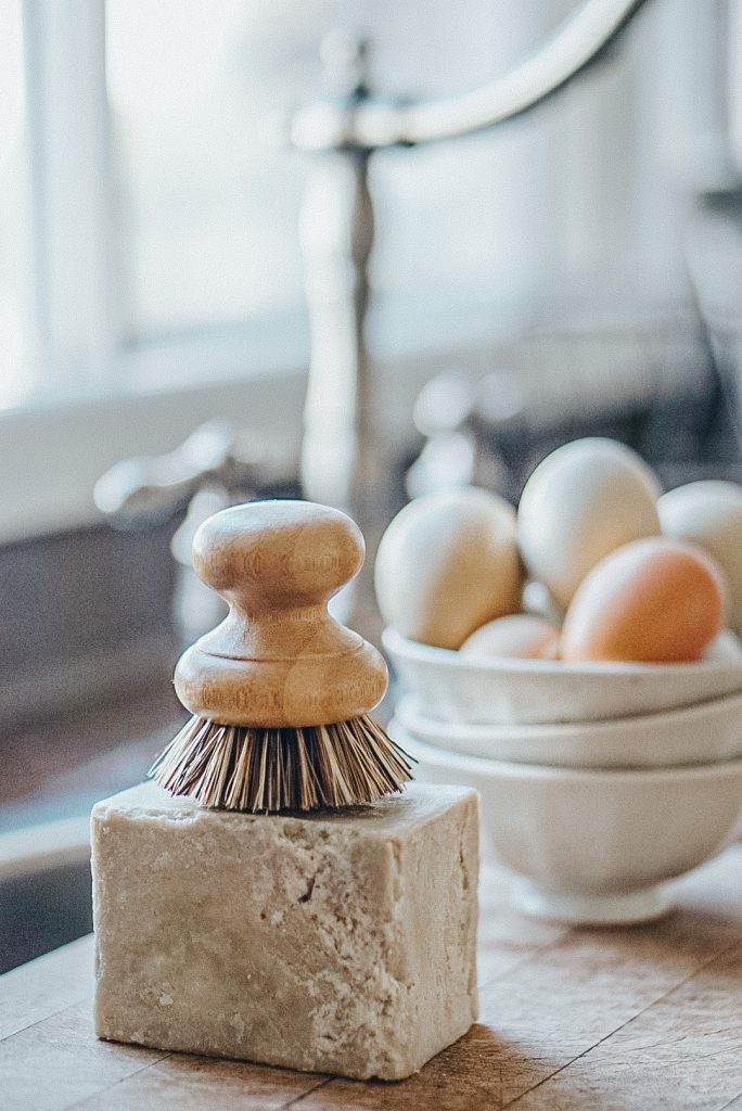 French soap with a scrub brush on top and farm fresh eggs in a bowl beside them.