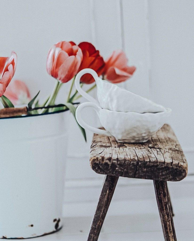 Hand pinched pottery mugs stacked on a wooden antique bench beside some tulips.