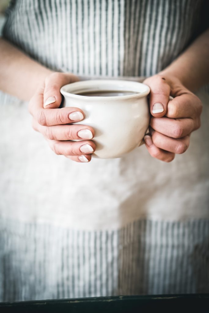 A woman holding a white stoneware mug in two hands.