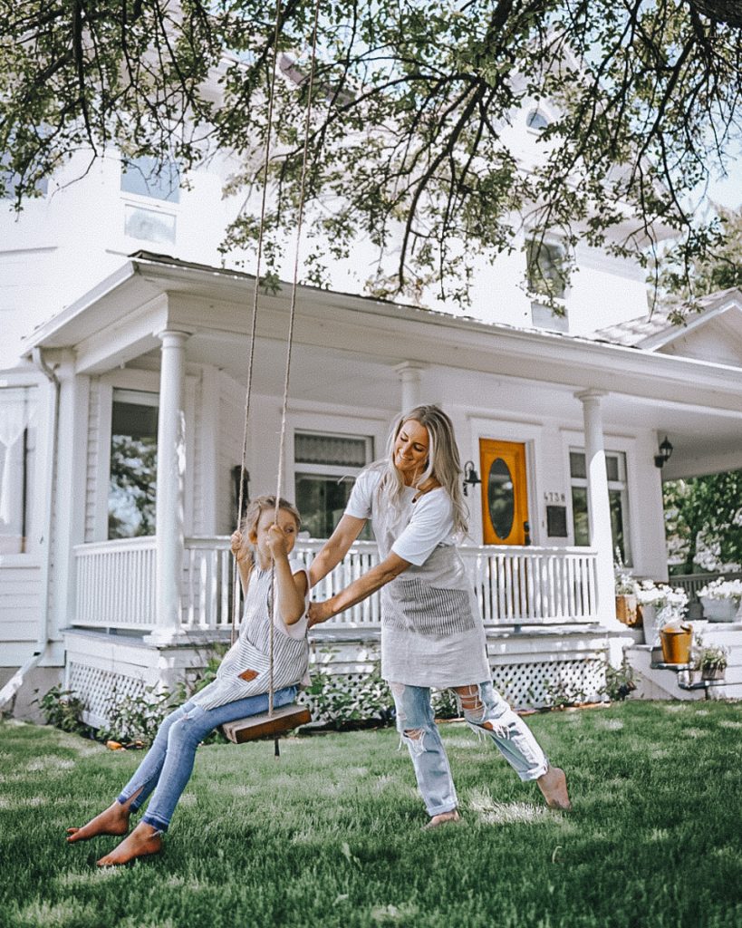 Deborah pushing her daughter on a swing in front of a beautiful white Victorian house. 