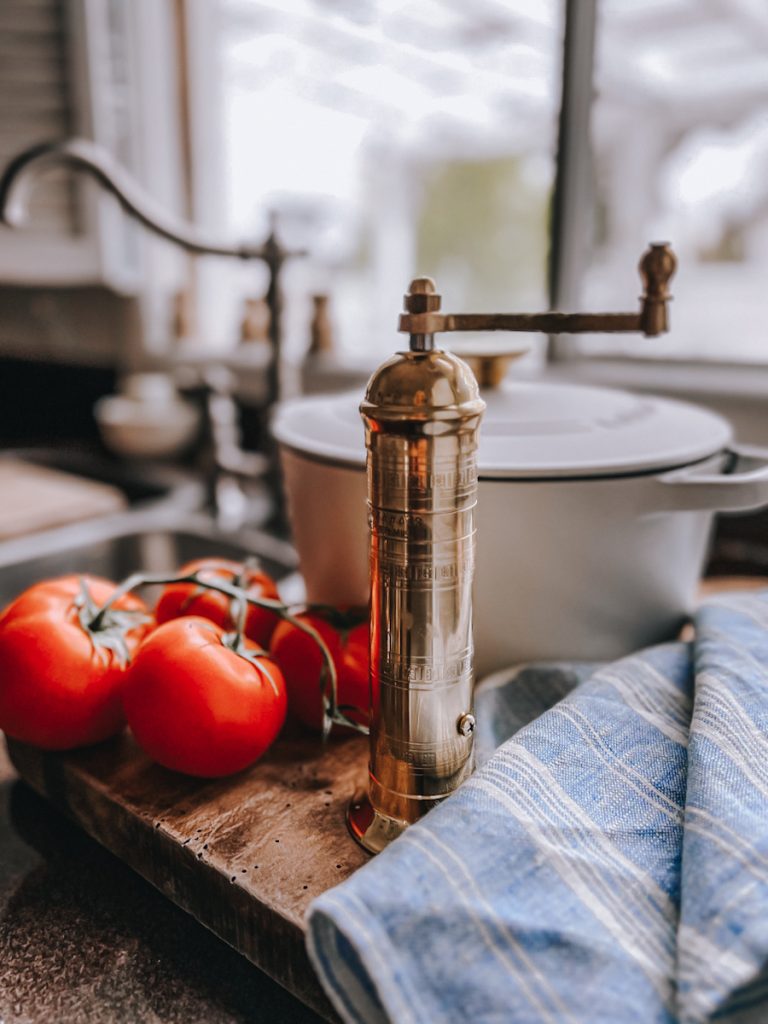 Brass pepper grinder beside on the counter next to tomatoes.