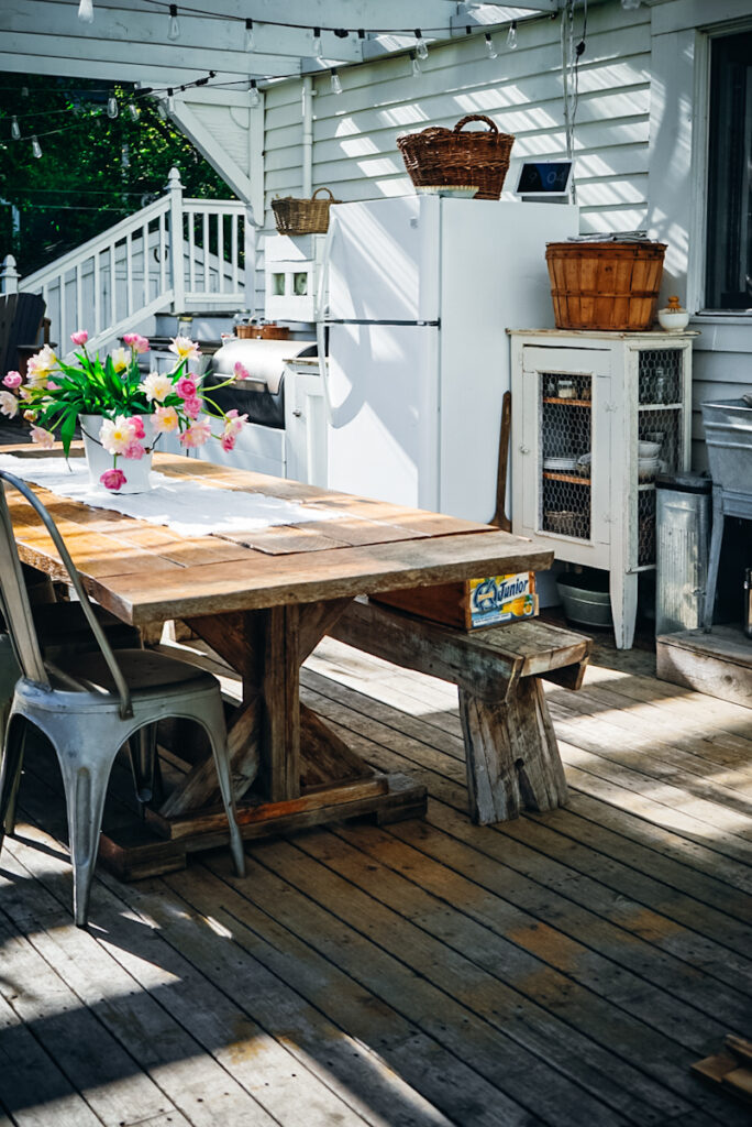 A beautiful farmhouse style small outdoor kitchen set up with a large wooden dining room table.