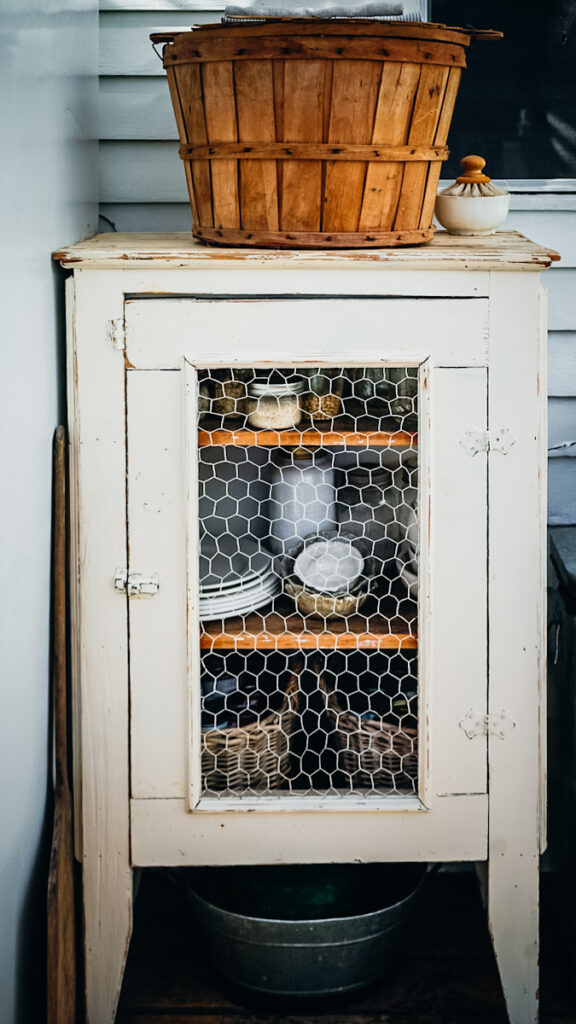 An antique pie cupboard being used for storage in a small outdoor kitchen.
