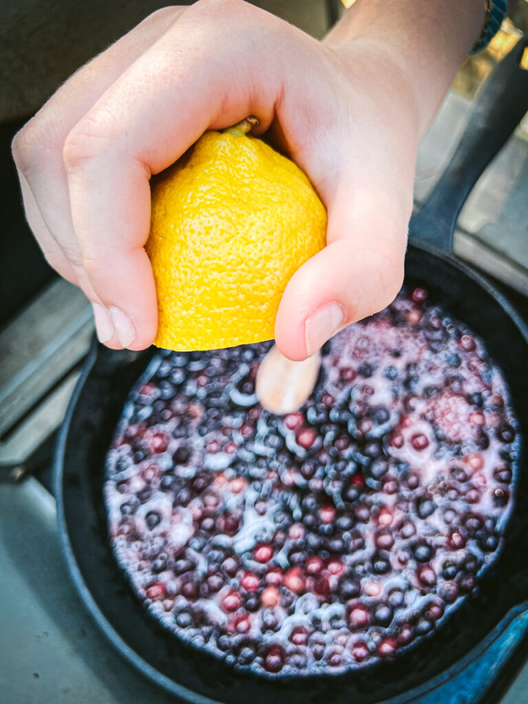 Adding lemon juice to a pan of simmering Saskatoon berries.