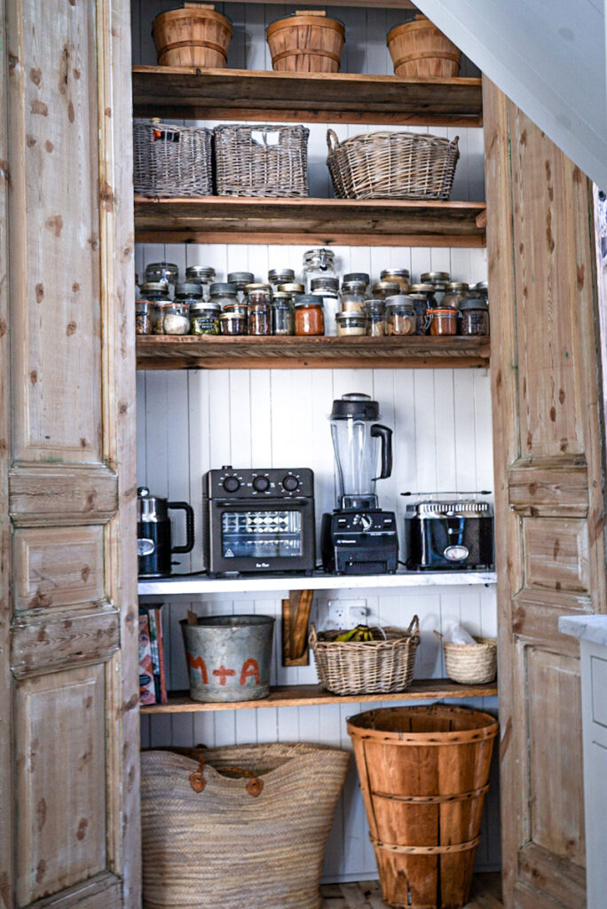 Large European style pantry with raw wood doors, dry food storage and small appliances.