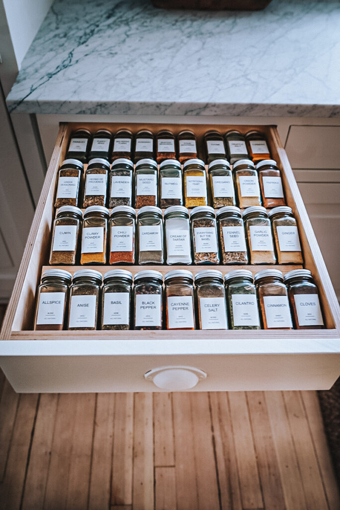 Organized spice drawer with all the spices in matching containers and in alphabetical order.