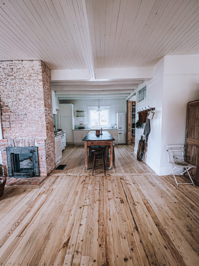 View of a beautiful open concept European kitchen with original hardwood floors and an exposed brick fireplace. 