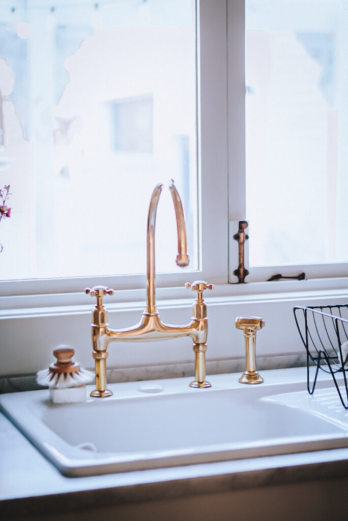 Beautiful brass faucet in a white cast iron sink in front of a European push and pull window.