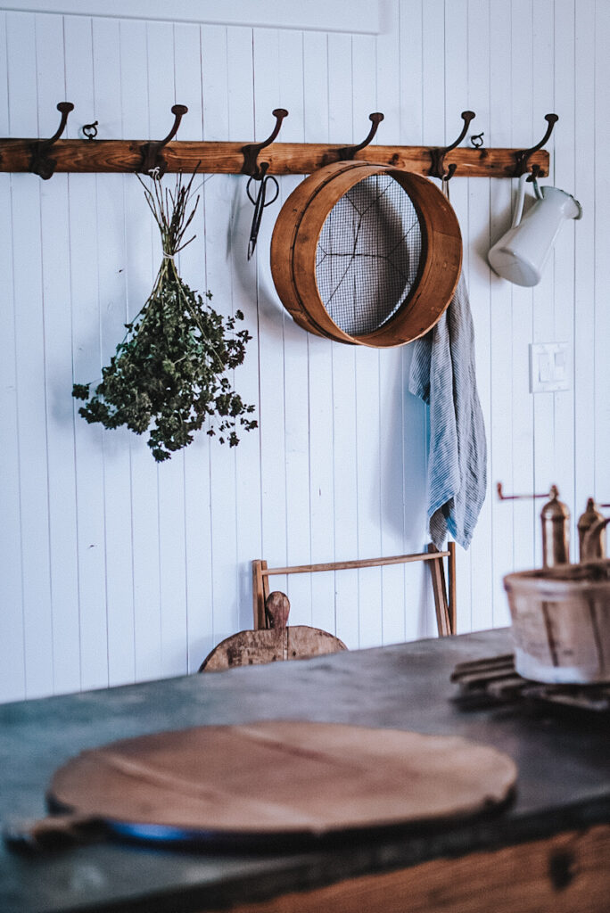 An antique French coat rack hanging in a Scandinavian ktichen with linens, antiques and drying herbs hanging from it.