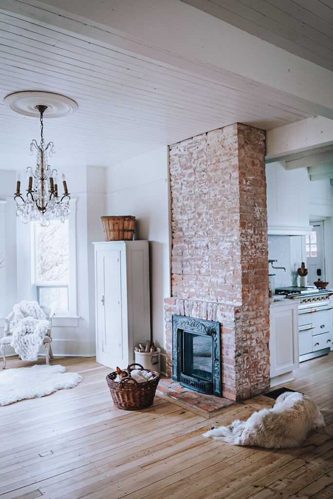 Cozy exposed brick fireplace in a beautiful white kitchen that has a Lanache stove.